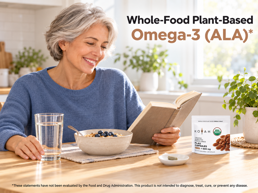 Woman smiling and reading at a breakfast table with a glass of water and a KOYAH Organic Sprouted Flax Capsules pouch: whole-food plant-based omega-3 (ALA)