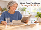 Woman smiling and reading at a breakfast table with a glass of water and a KOYAH Organic Sprouted Flax Capsules pouch: whole-food plant-based omega-3 (ALA)