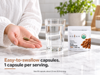 Hand holding a single KOYAH Organic Sprouted Flax Capsule next to the pouch and a glass of water: easy-to-swallow capsules, 1 capsule per serving